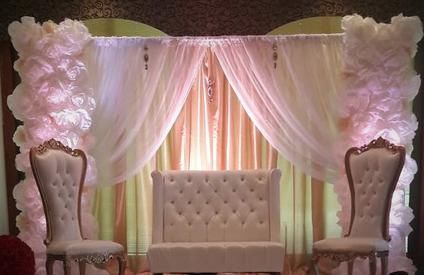 There is a couch and two chairs in front of a pink curtain.