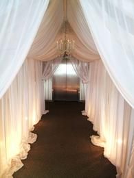 A hallway with white curtains and a chandelier.