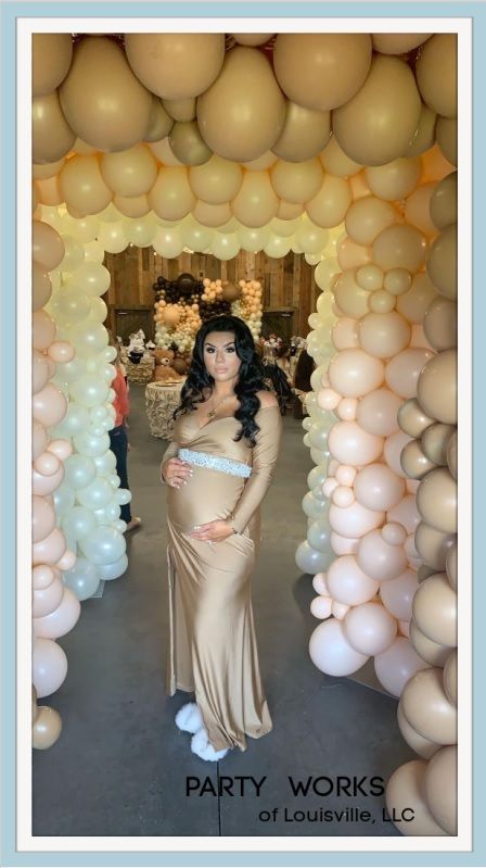 A pregnant woman is standing in front of a wall of balloons.