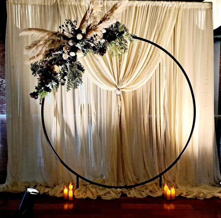 A circular arch with flowers and candles in front of a white curtain.