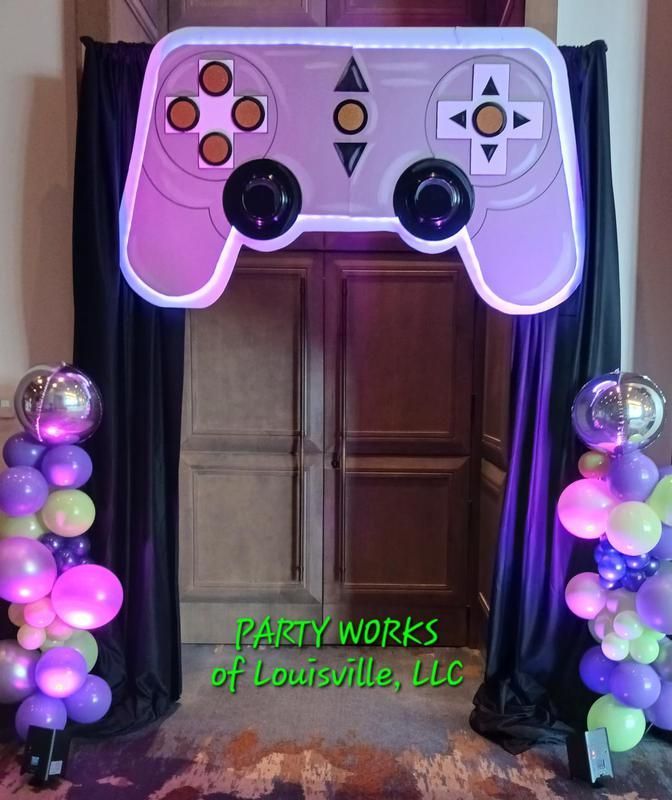 A video game controller is surrounded by purple and green balloons