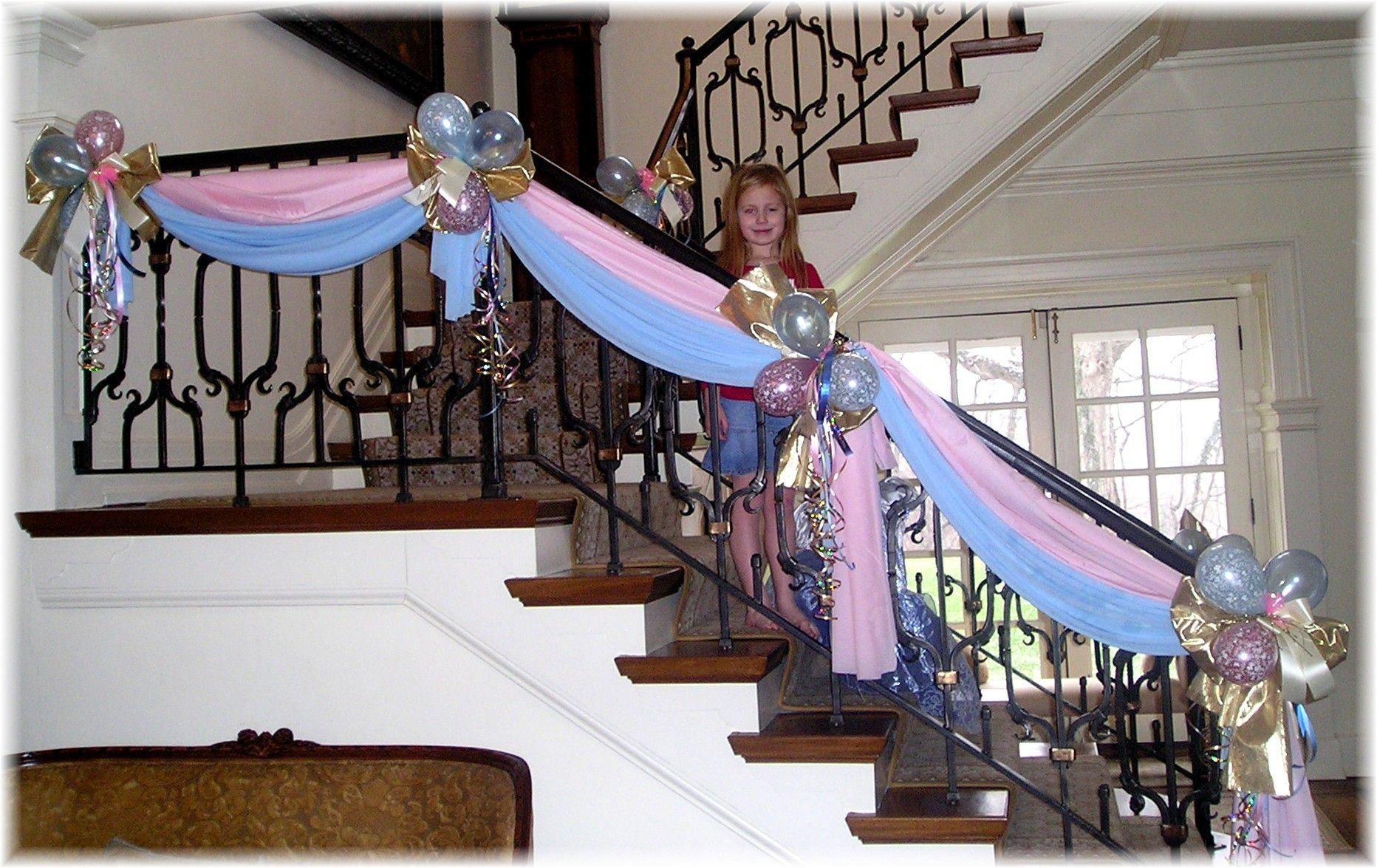 A girl is standing on a staircase decorated with pink and blue balloons
