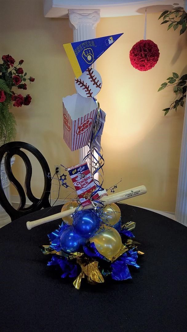 A baseball centerpiece with balloons and a bat on a table.