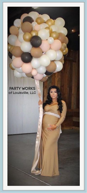 A pregnant woman in a long dress is holding a bunch of balloons.