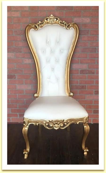A white and gold chair is sitting in front of a brick wall.
