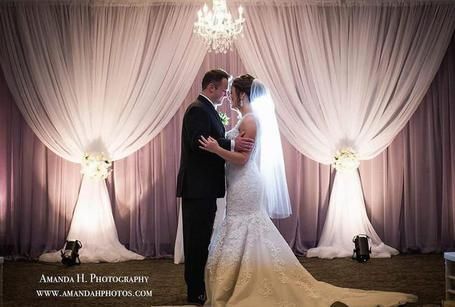 A bride and groom are standing in front of a white curtain.