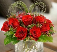 A vase filled with red roses and greenery on a table.