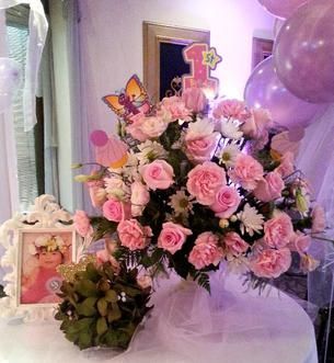 A table topped with pink flowers and balloons for a baby 's first birthday.