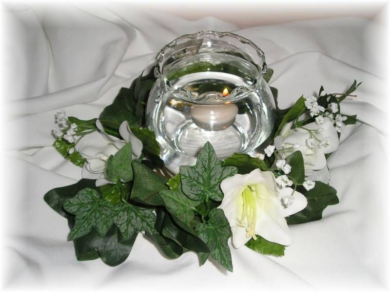 A candle in a glass surrounded by flowers and leaves