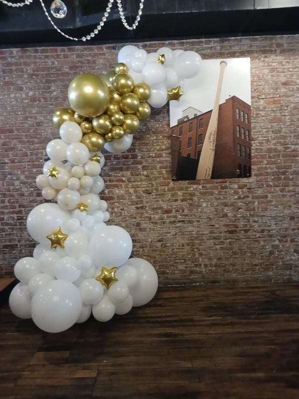 A bunch of white and gold balloons are hanging on a brick wall.