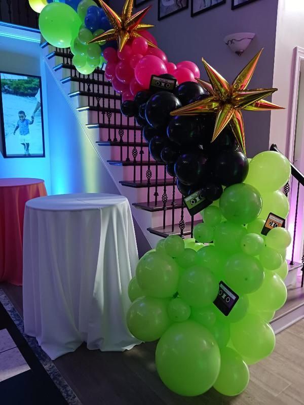 A bunch of balloons are sitting on a table in front of a staircase.