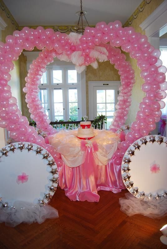 A table with a cake on it is surrounded by pink balloons in the shape of a carriage