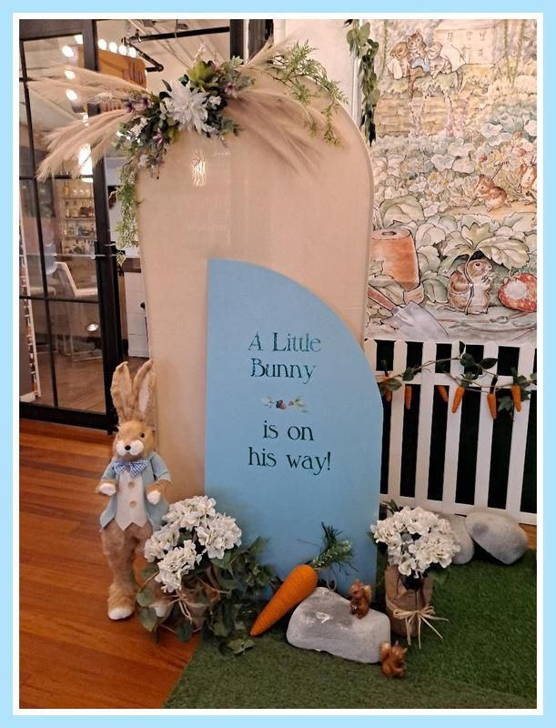 A sign that says `` a little bunny is on his way '' is surrounded by flowers and carrots.
