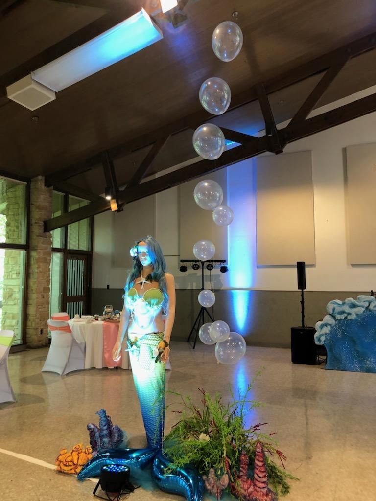 A mermaid statue in a room with balloons hanging from the ceiling.