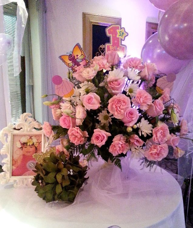 A vase of pink flowers sits on a table next to balloons and a picture frame