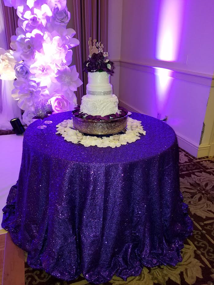 A wedding cake is sitting on a table with a purple table cloth.
