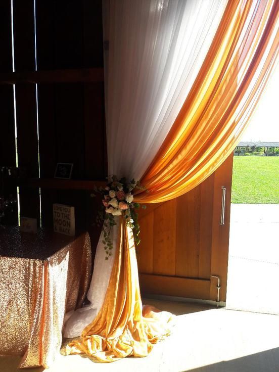 A table with a table cloth and flowers behind a curtain in a barn.