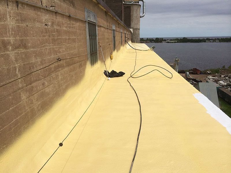 Exterior view of a building's yellow roof with cables, a brick wall, and a body of water in the background.