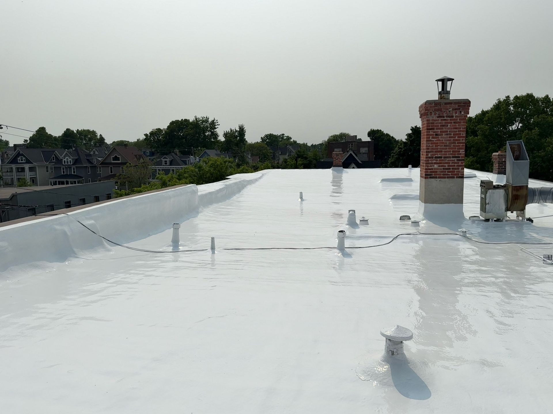 White, reflective roof surface with pipes and a brick chimney, in an outdoor setting on a sunny day.