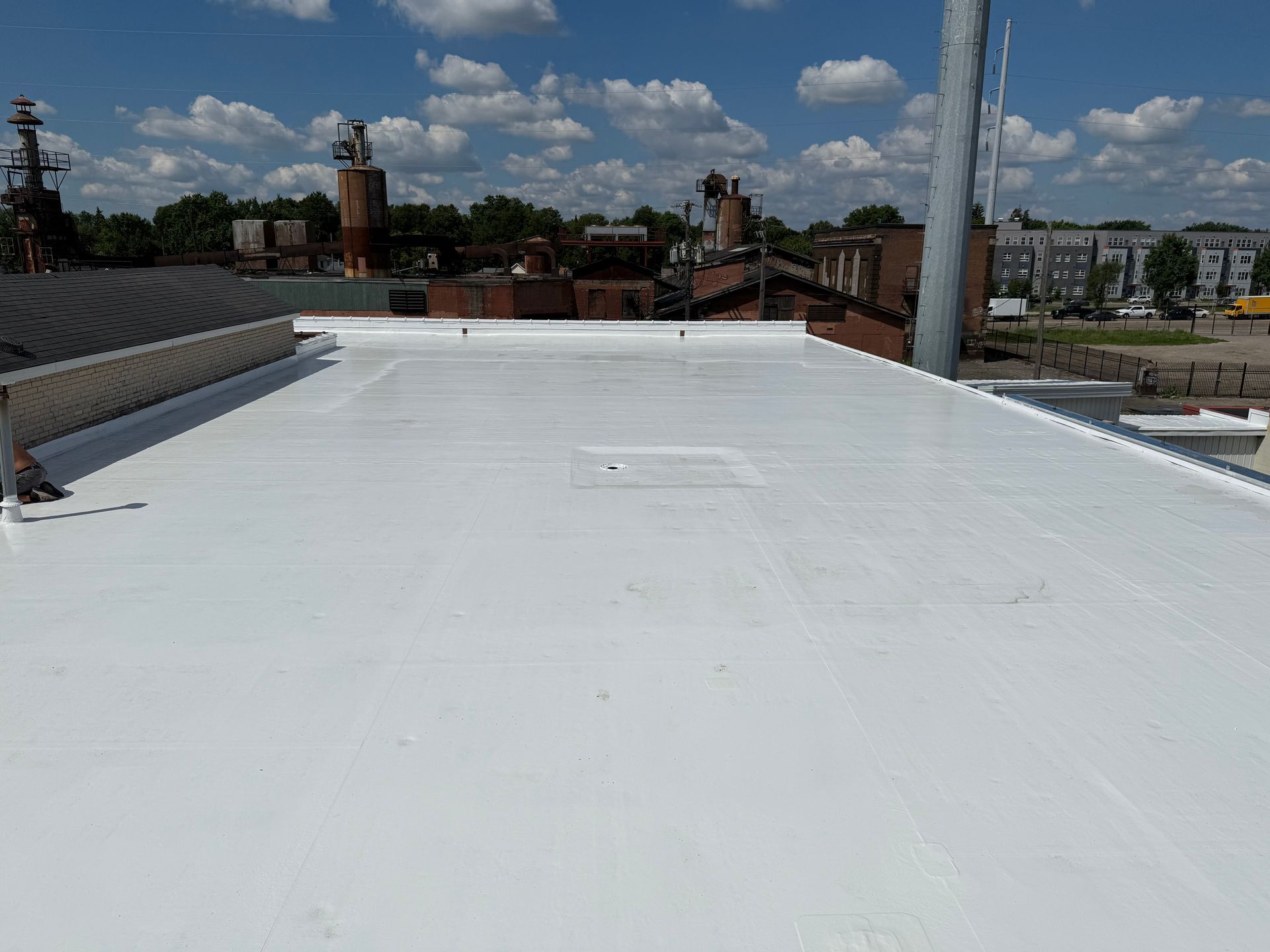 White flat roof with industrial buildings in background, blue sky.