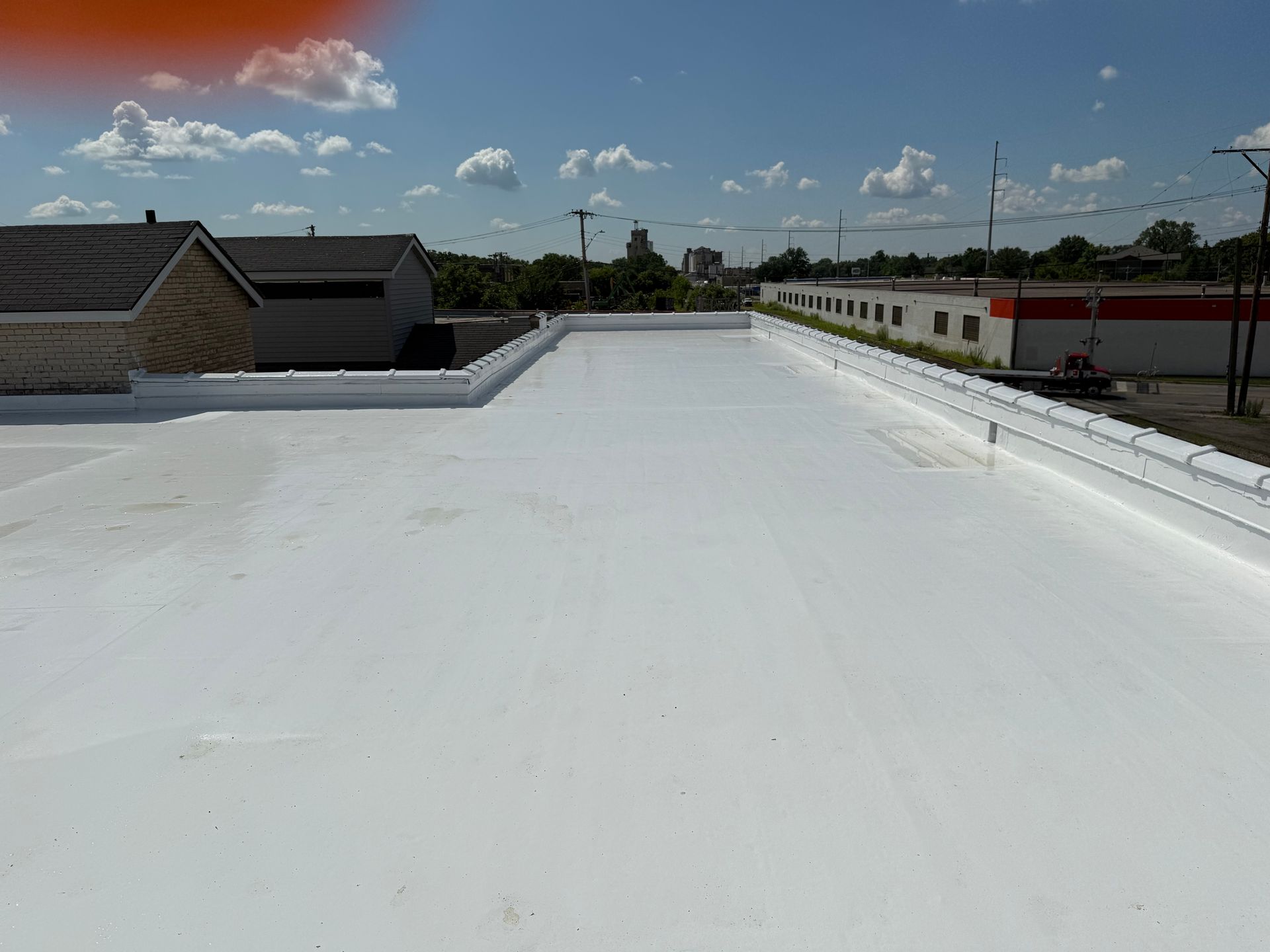 White flat commercial roof under a blue sky, with surrounding buildings.