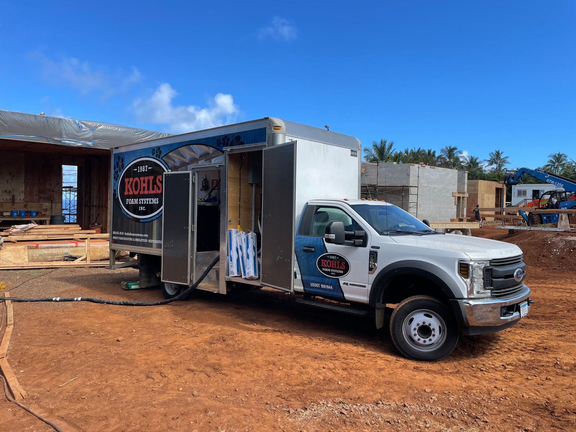White truck with toolbox body at a construction site, blue logo on the door.