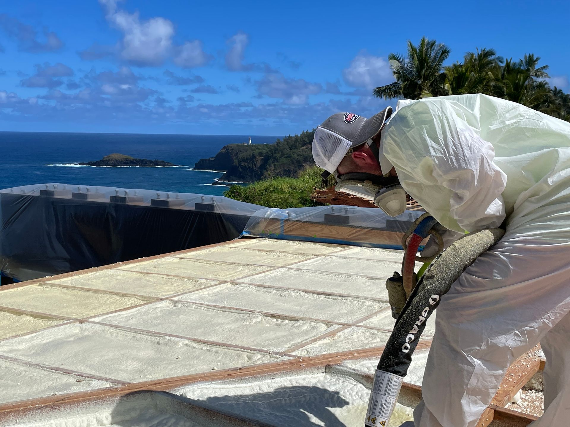 Person spraying foam insulation on a roof with ocean view.