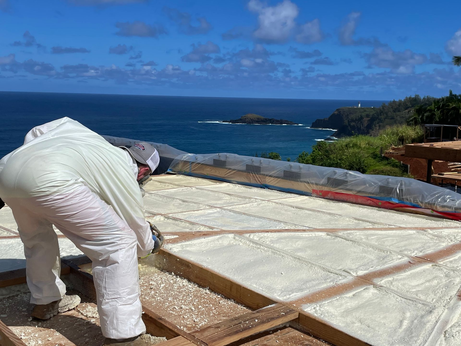 Person spraying foam insulation on a roof overlooking the ocean.