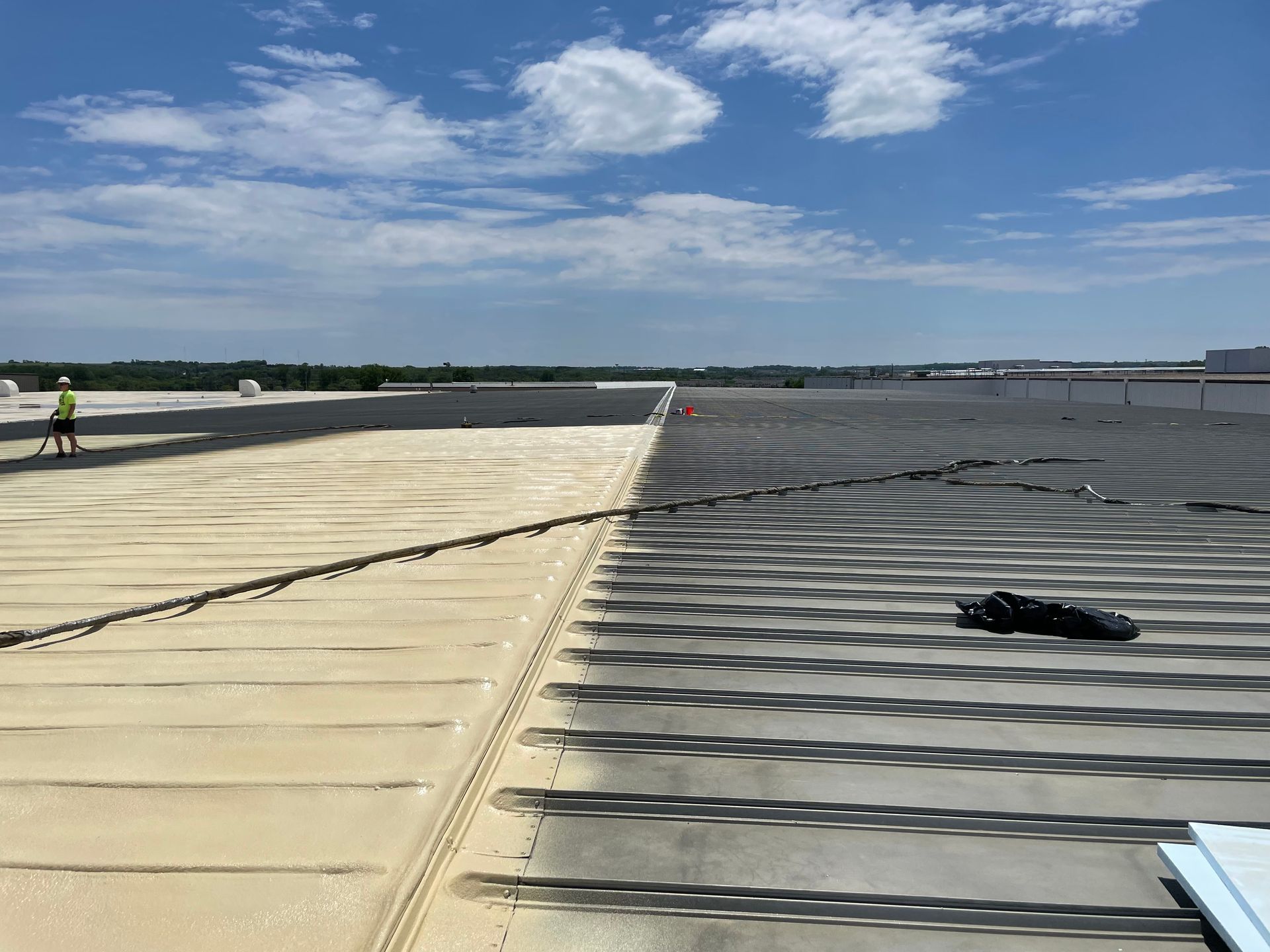 Rooftop with light tan and dark gray sections; worker in distance, blue sky with clouds.
