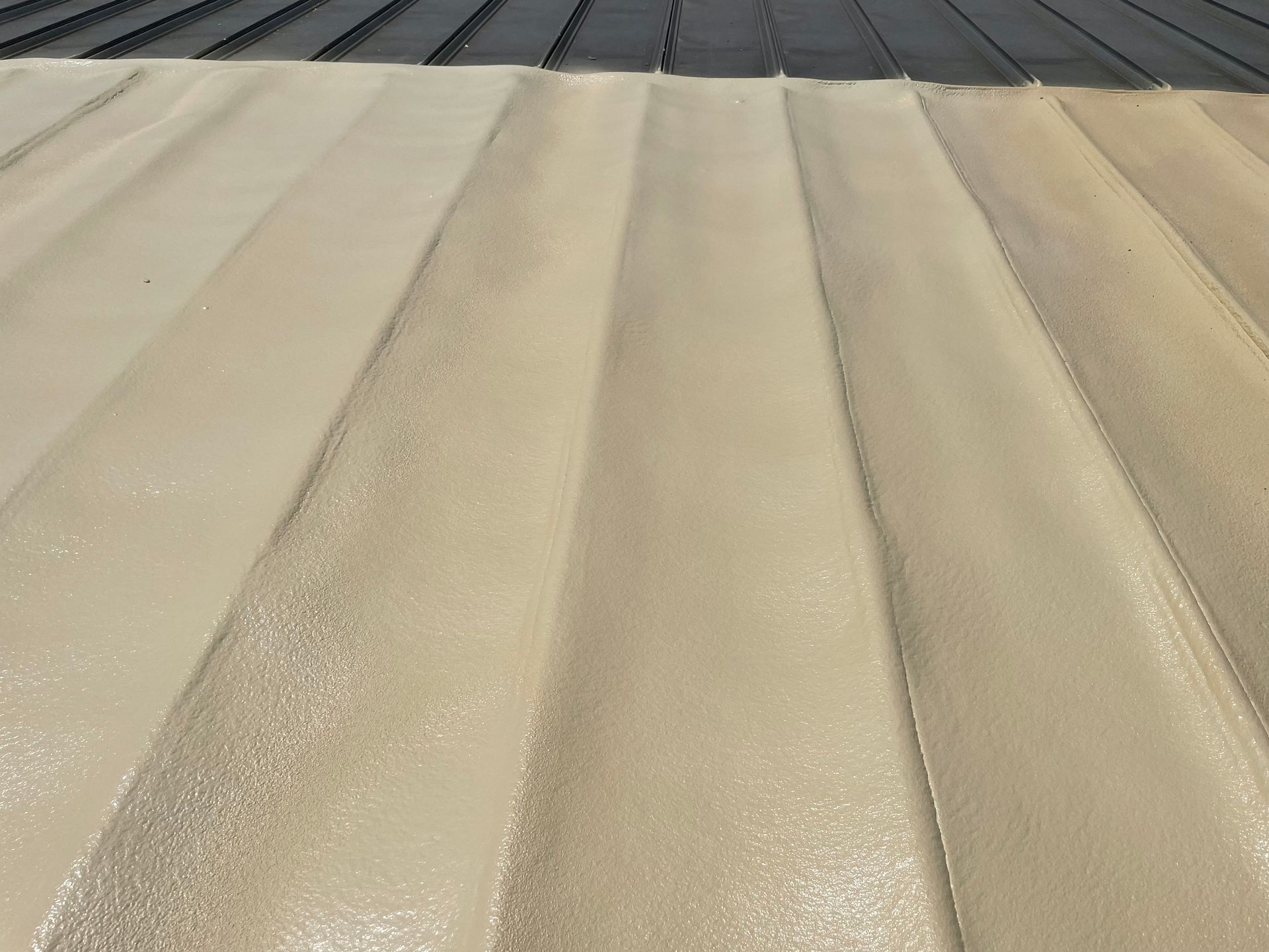 Cream-colored coating applied to a corrugated metal roof, transitioning to black at the top.