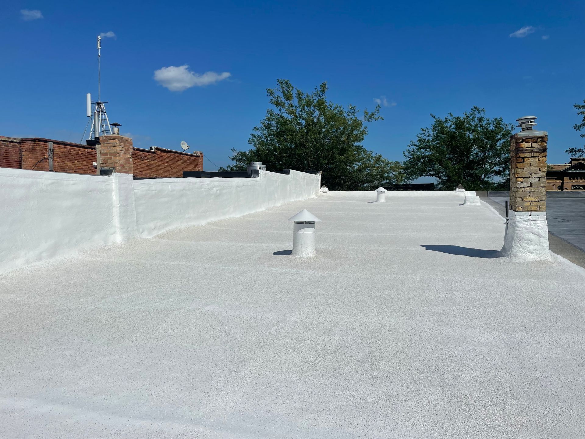 White coated flat roof with chimneys, vents, and blue sky.