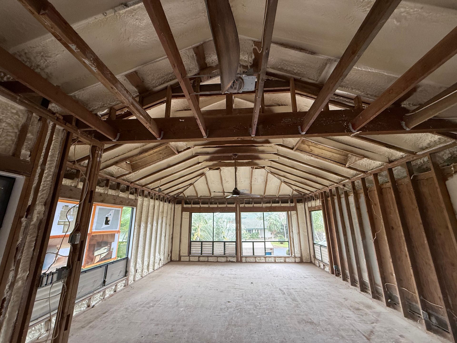 Interior of a room under construction with exposed wooden beams, foam insulation, and windows.