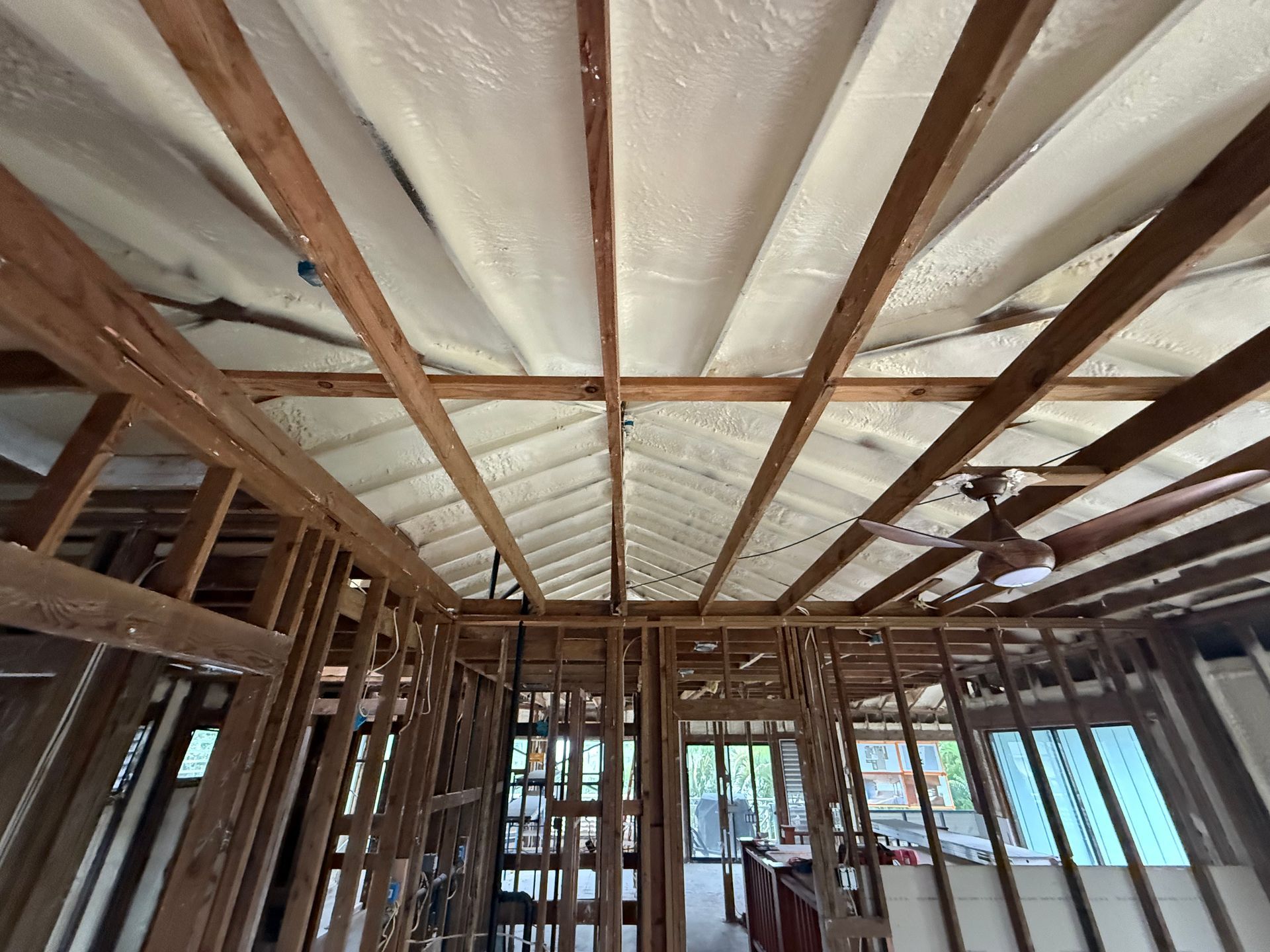 Interior view of a building under construction, showing exposed wooden beams and spray foam insulation.