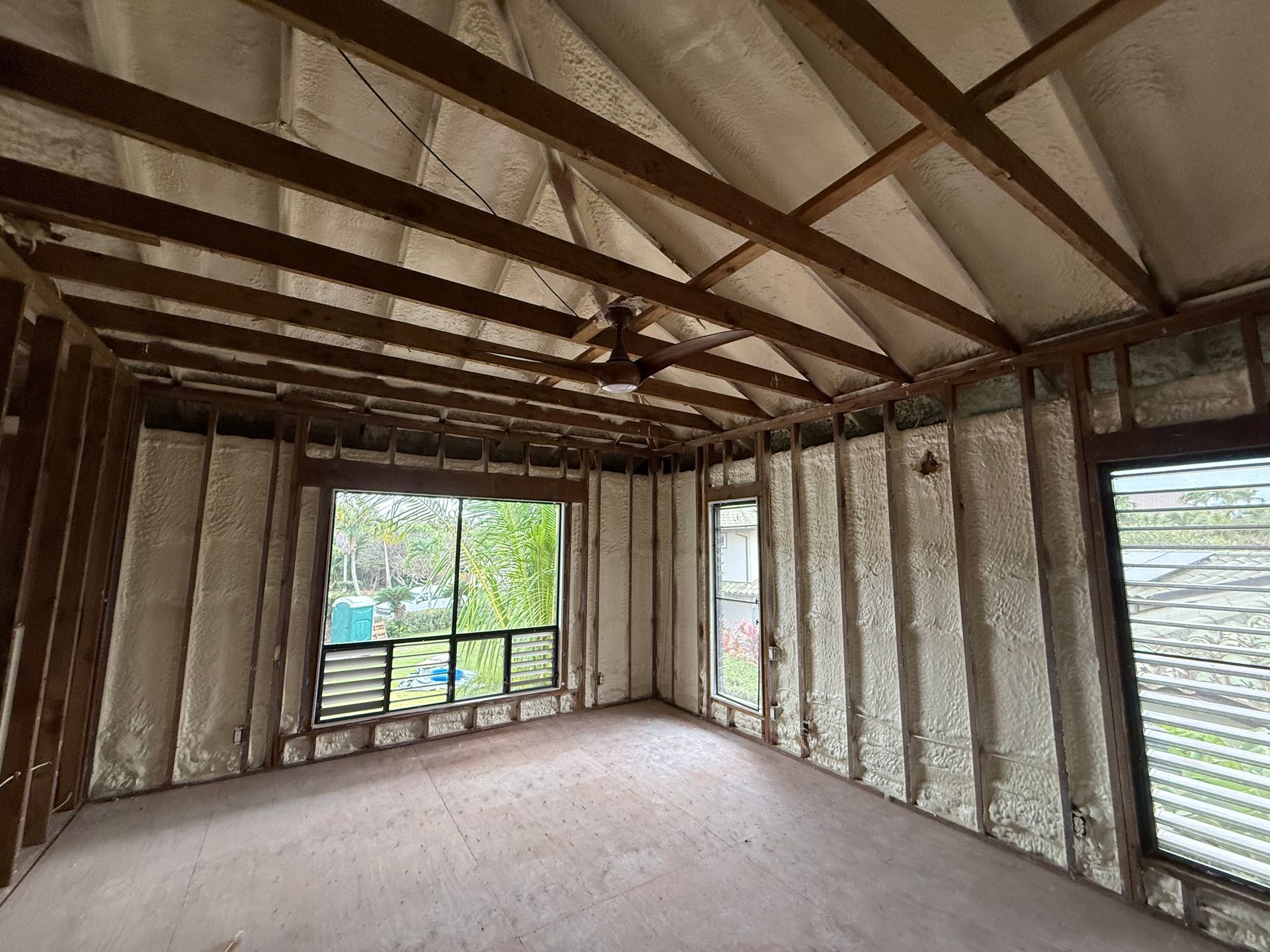 Interior of a room under construction, with exposed wooden beams, foam insulation, and windows.