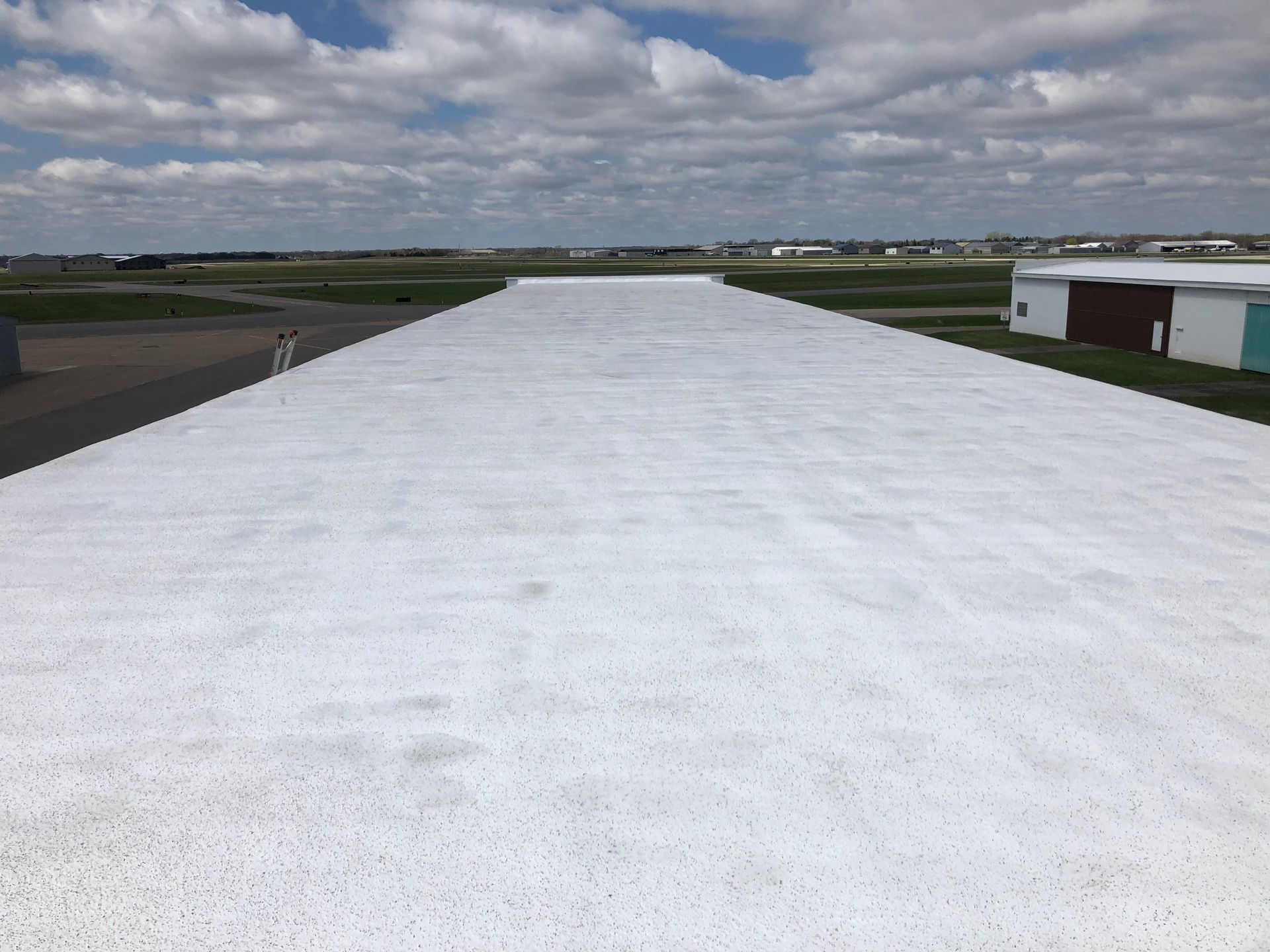 White runway at an airport, blue sky with clouds. Buildings and the horizon are visible.