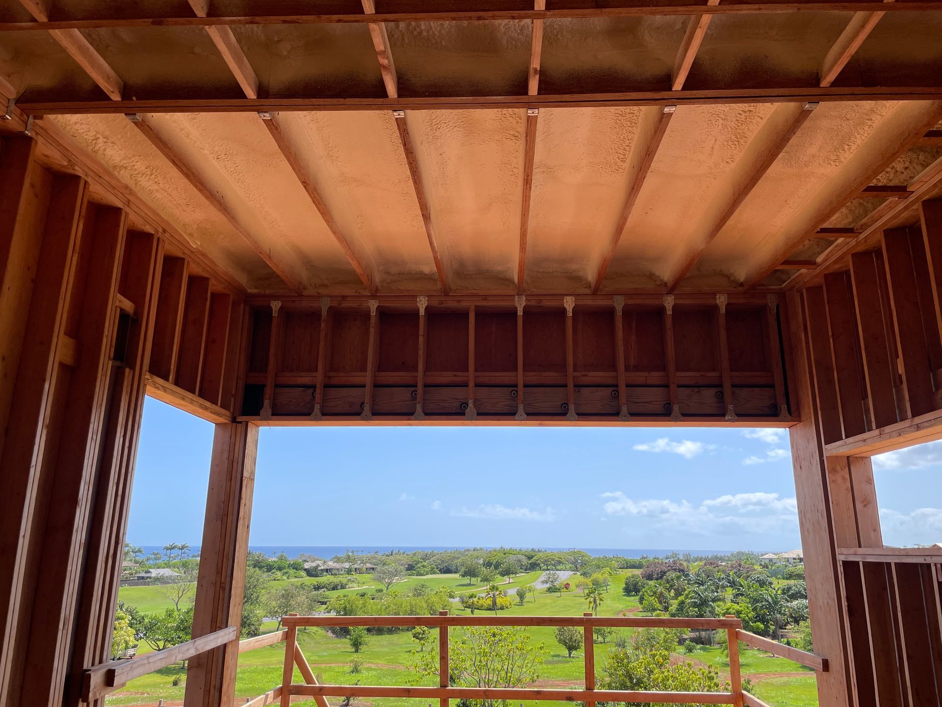 Wooden frame of a building in progress with a view of green fields and blue sky.