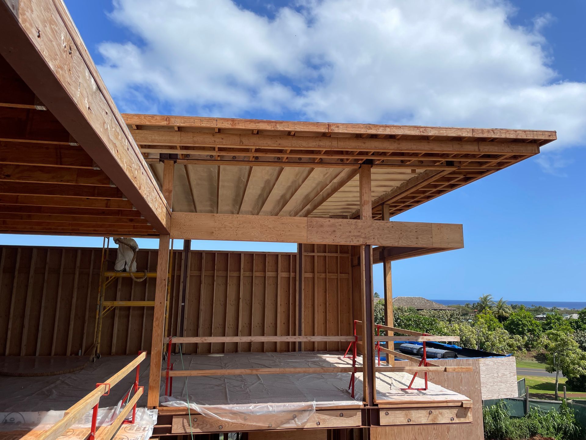 Wooden building under construction with exposed beams, blue sky and ocean view in background.