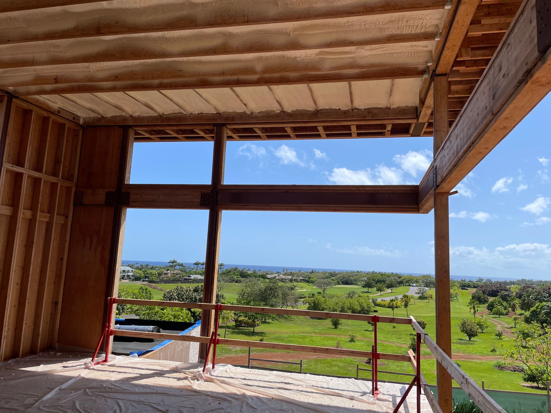 Interior view of a building under construction, open to a scenic landscape, framing a view of green fields, trees, and sky.