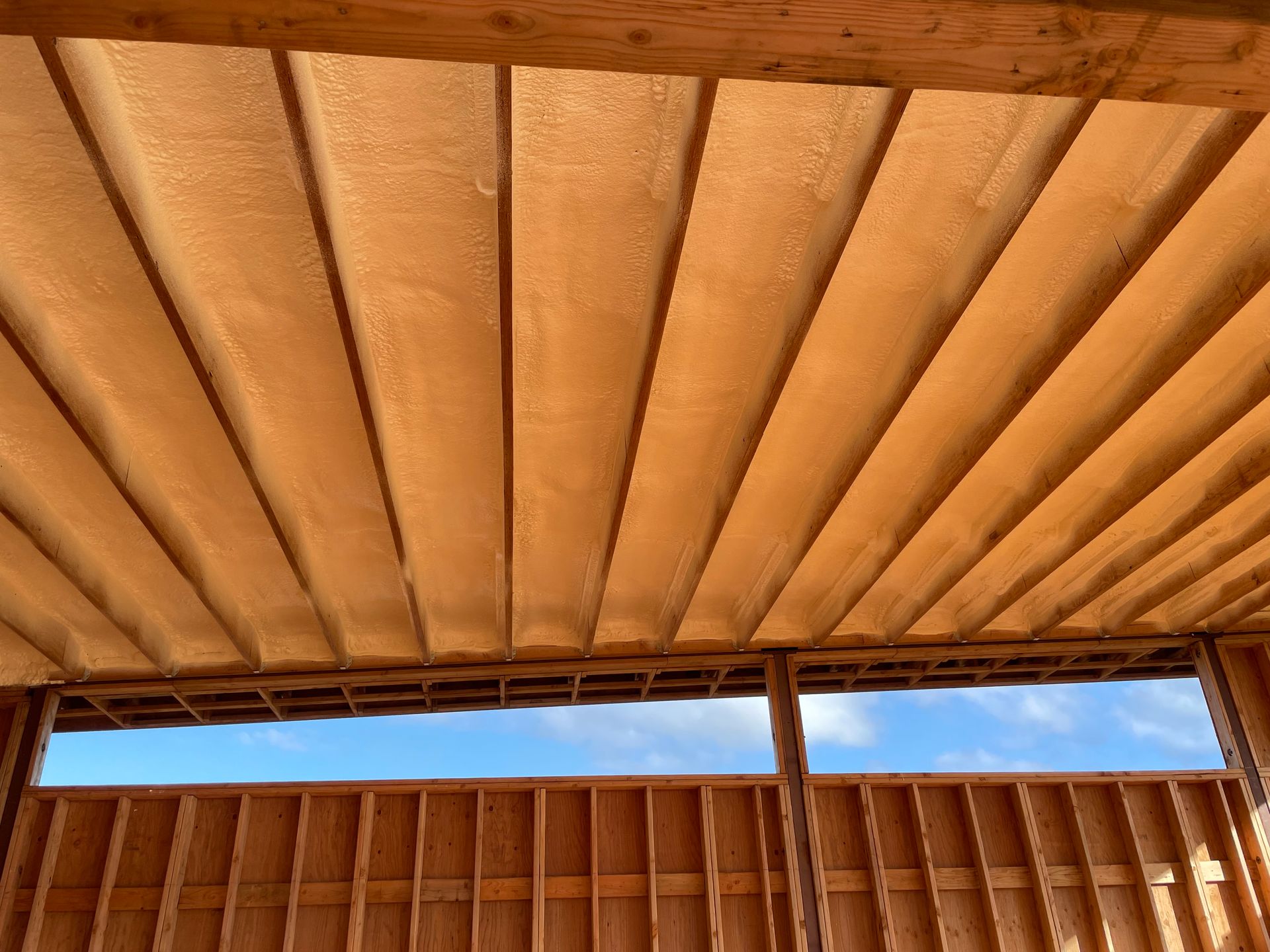 Wooden ceiling with beams, looking out to a blue sky through a wall under construction.