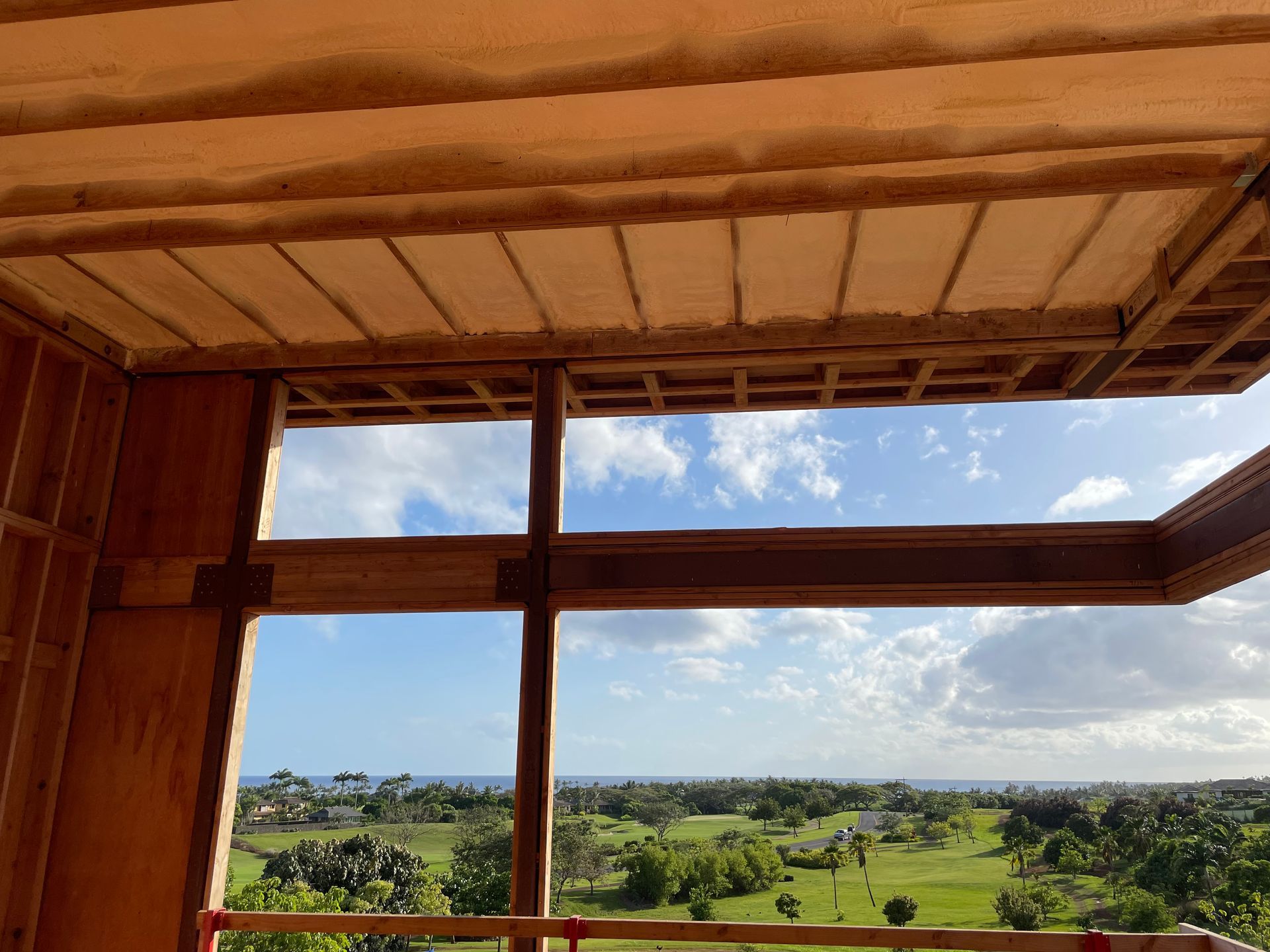Wooden building frame with open window overlooking a green landscape and blue sky.