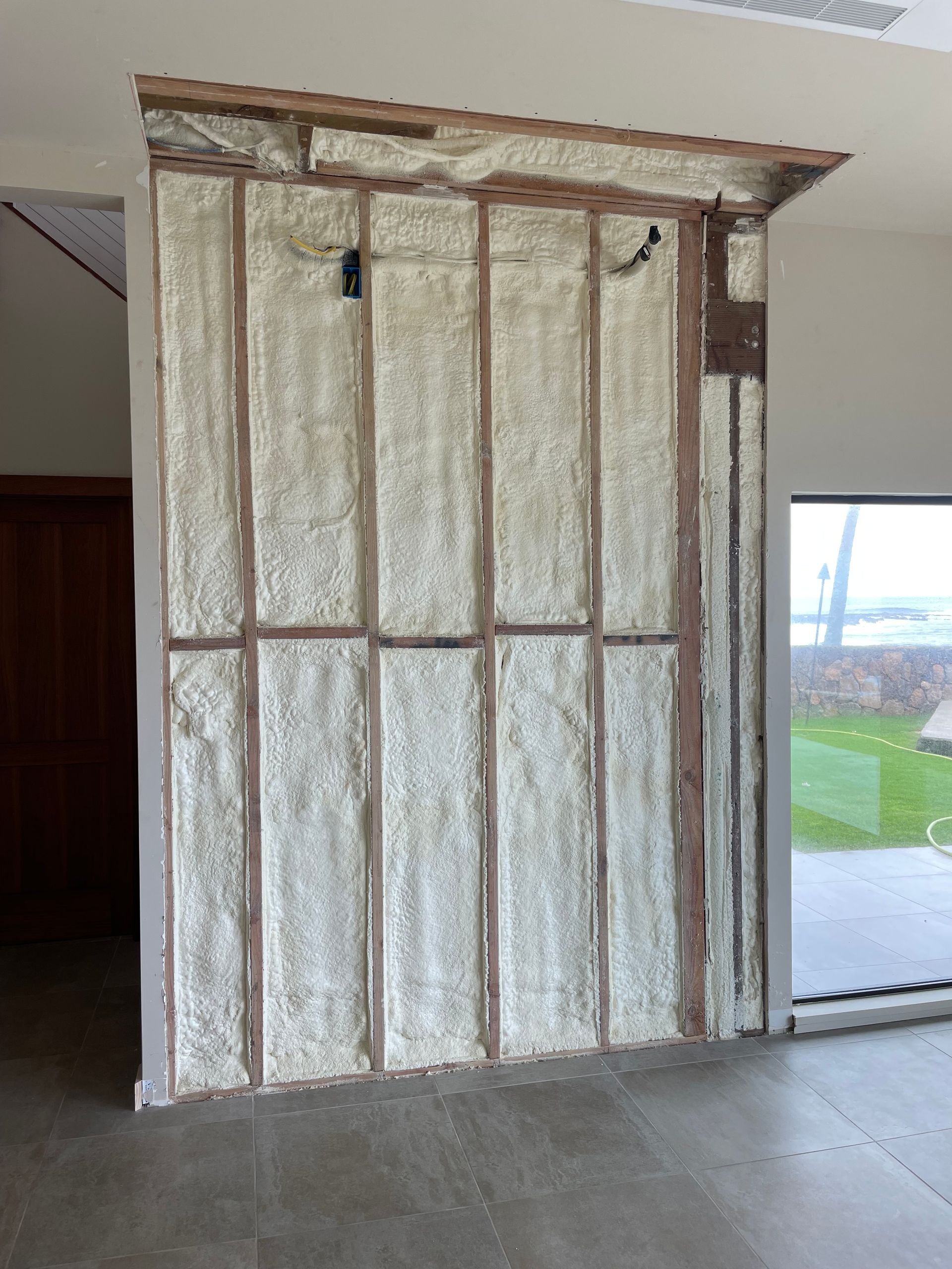 Interior wall under construction with exposed wooden frame and spray foam insulation.