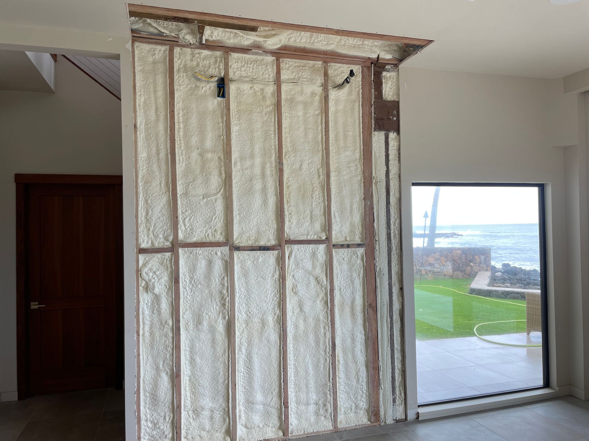 Wall with insulation between wooden studs; unfinished construction in a room with door and window.
