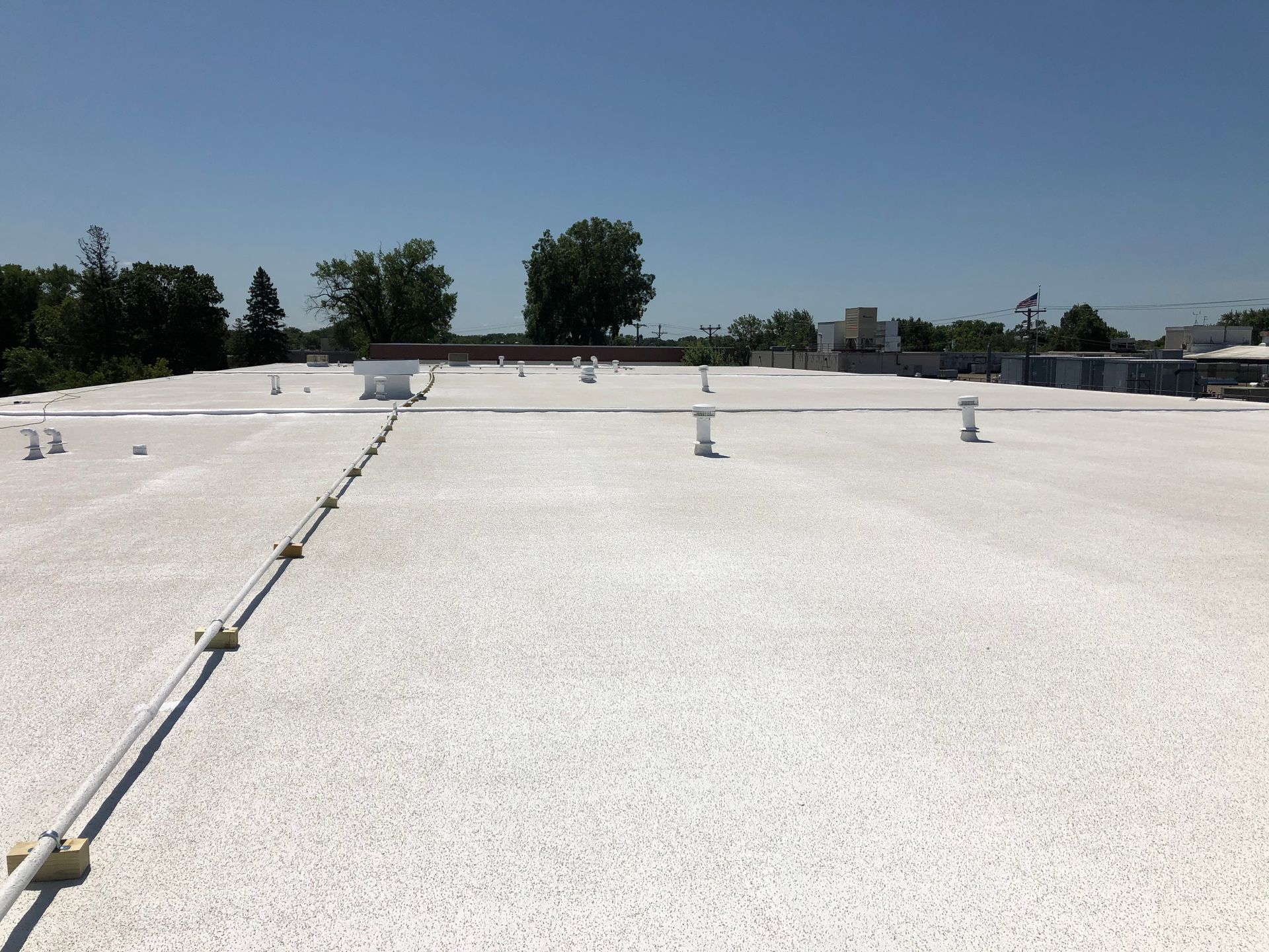 White, textured rooftop with vent pipes, under a bright blue sky.