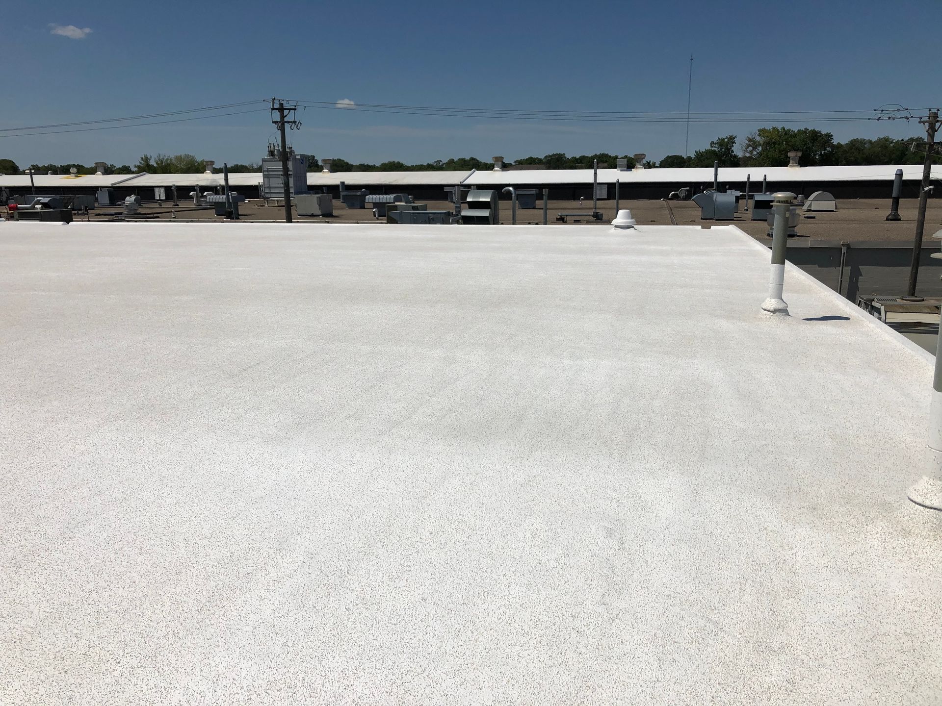 White commercial roof on a sunny day with utility poles and a parking area in the background.