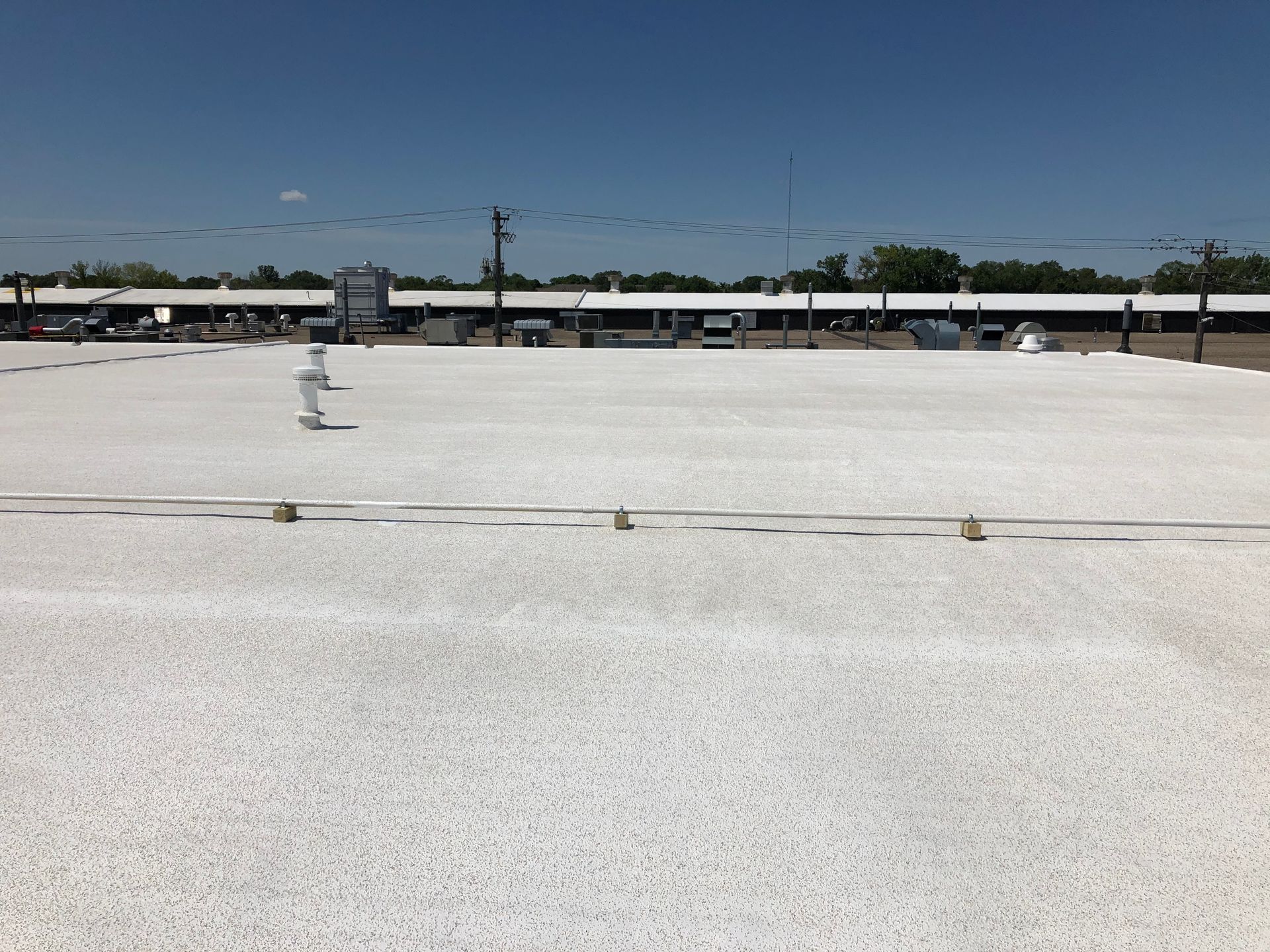 Flat white roof with several small fixtures against a blue sky, buildings in the background.