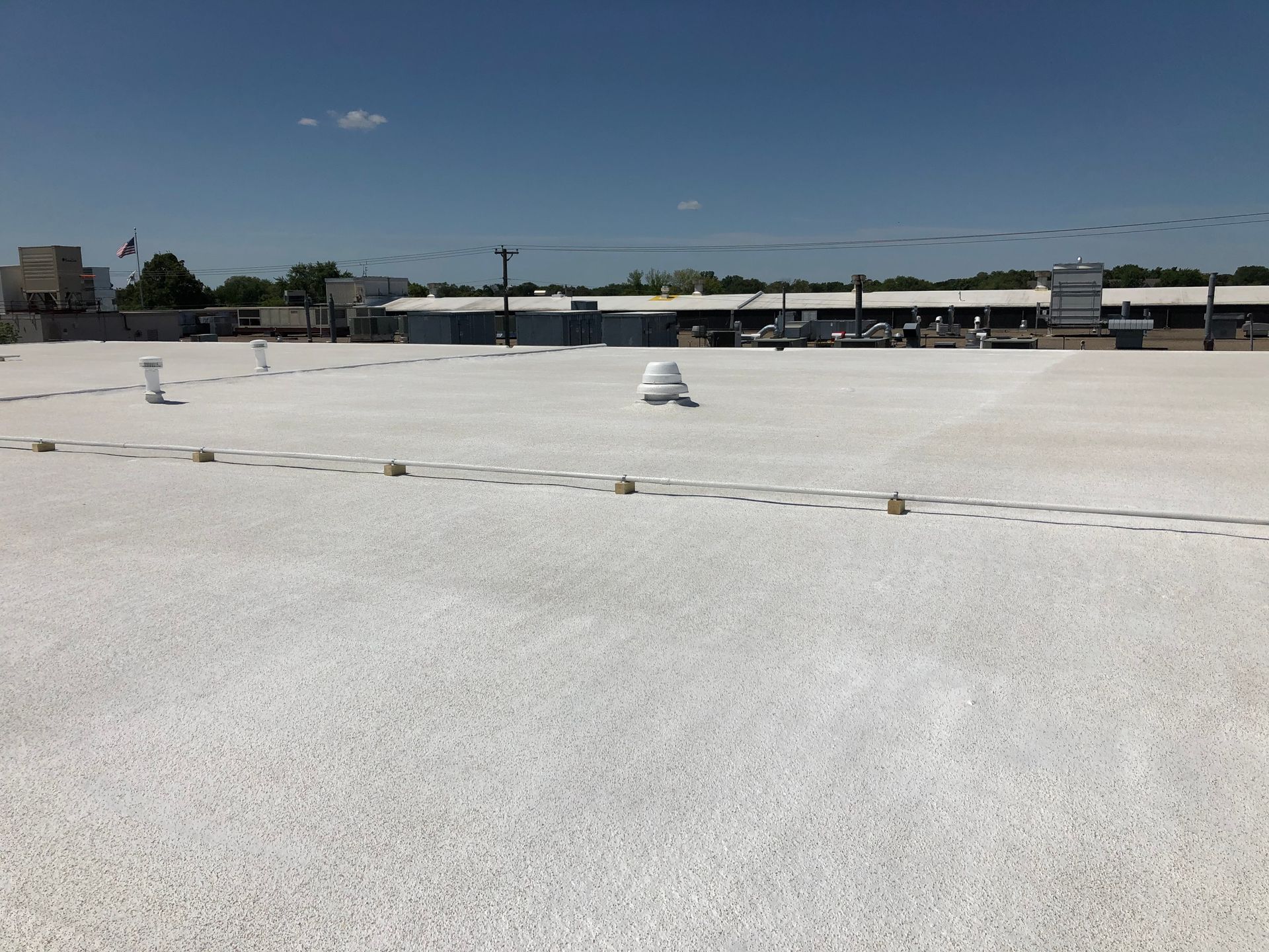 White rooftop under a blue sky, with some vents and a distant view of buildings.