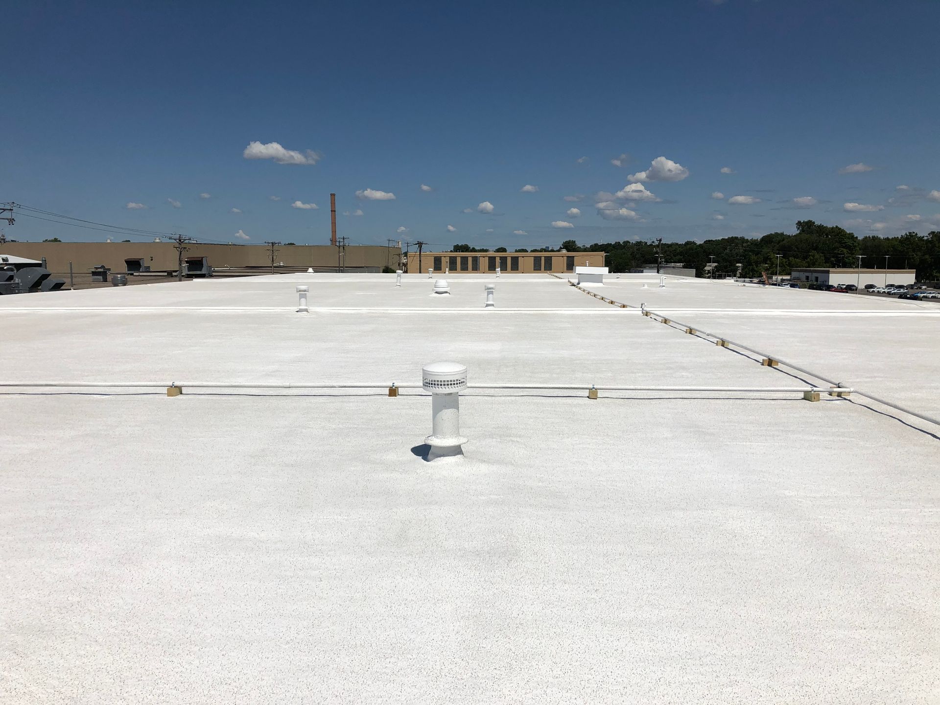 White commercial roof on a sunny day with blue sky and a distant building.