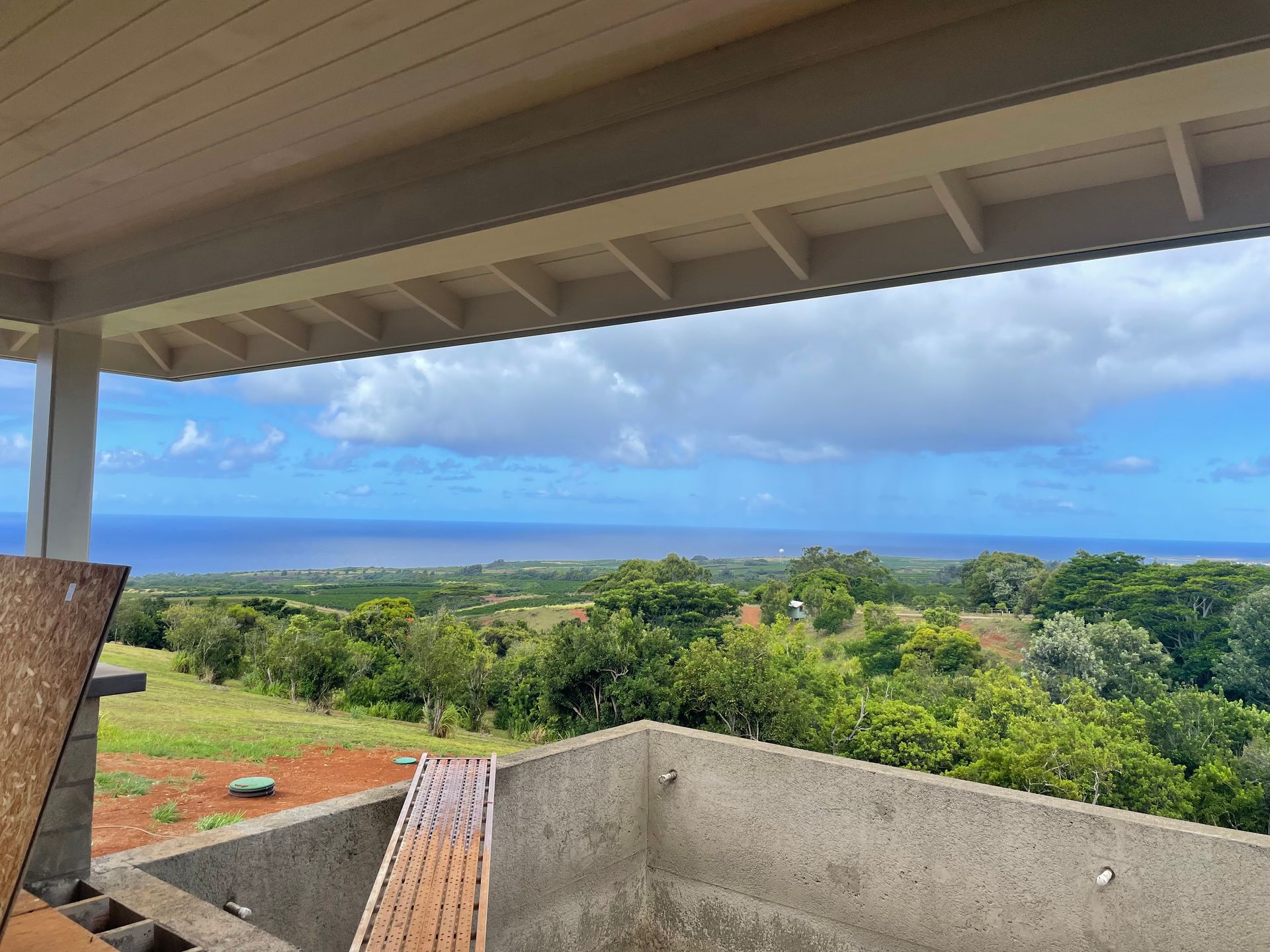 View from covered patio overlooking lush green landscape and ocean under blue sky.