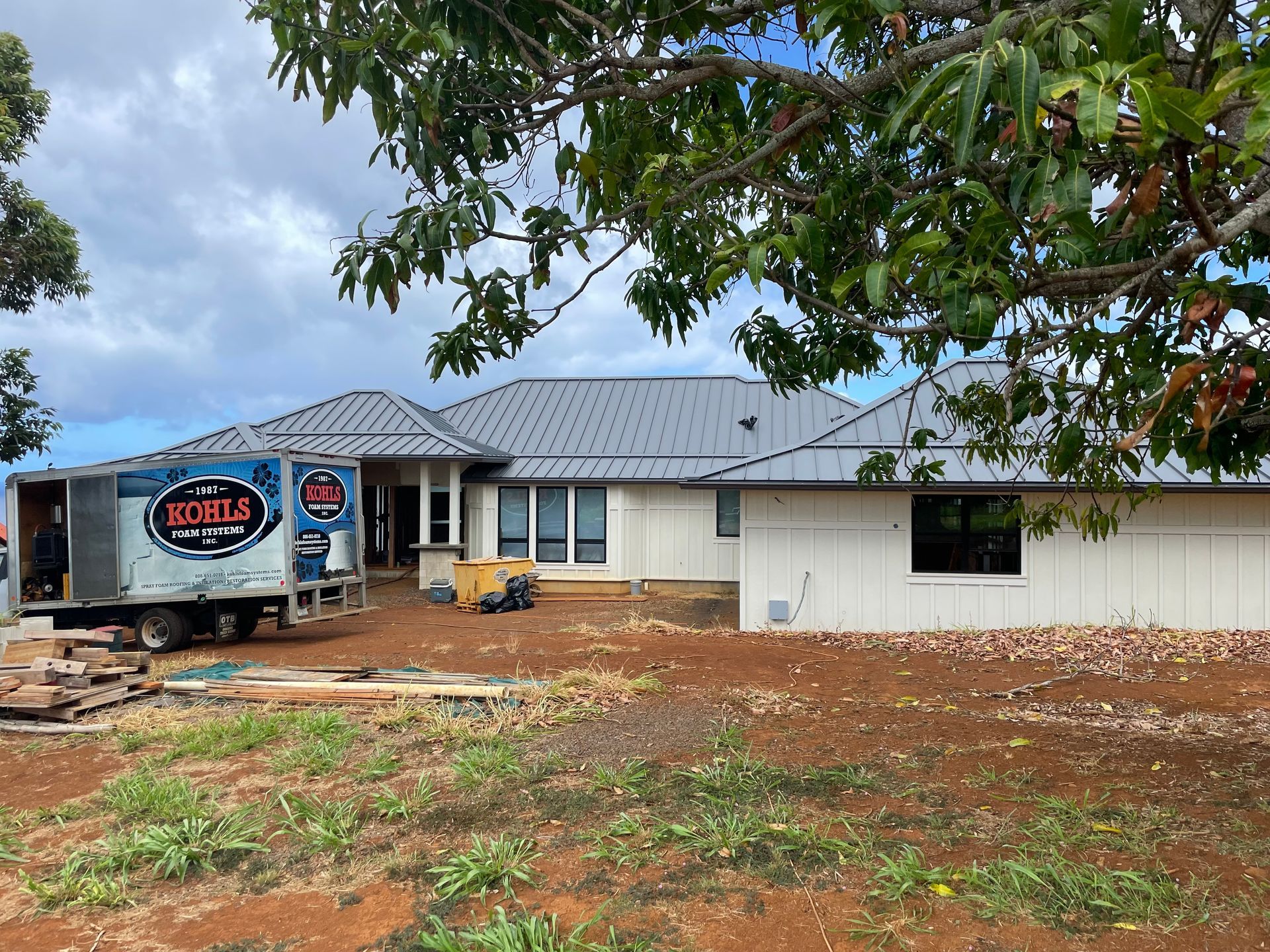 A low-rise house with a metal roof. A truck with a logo sits near the house on a lawn.