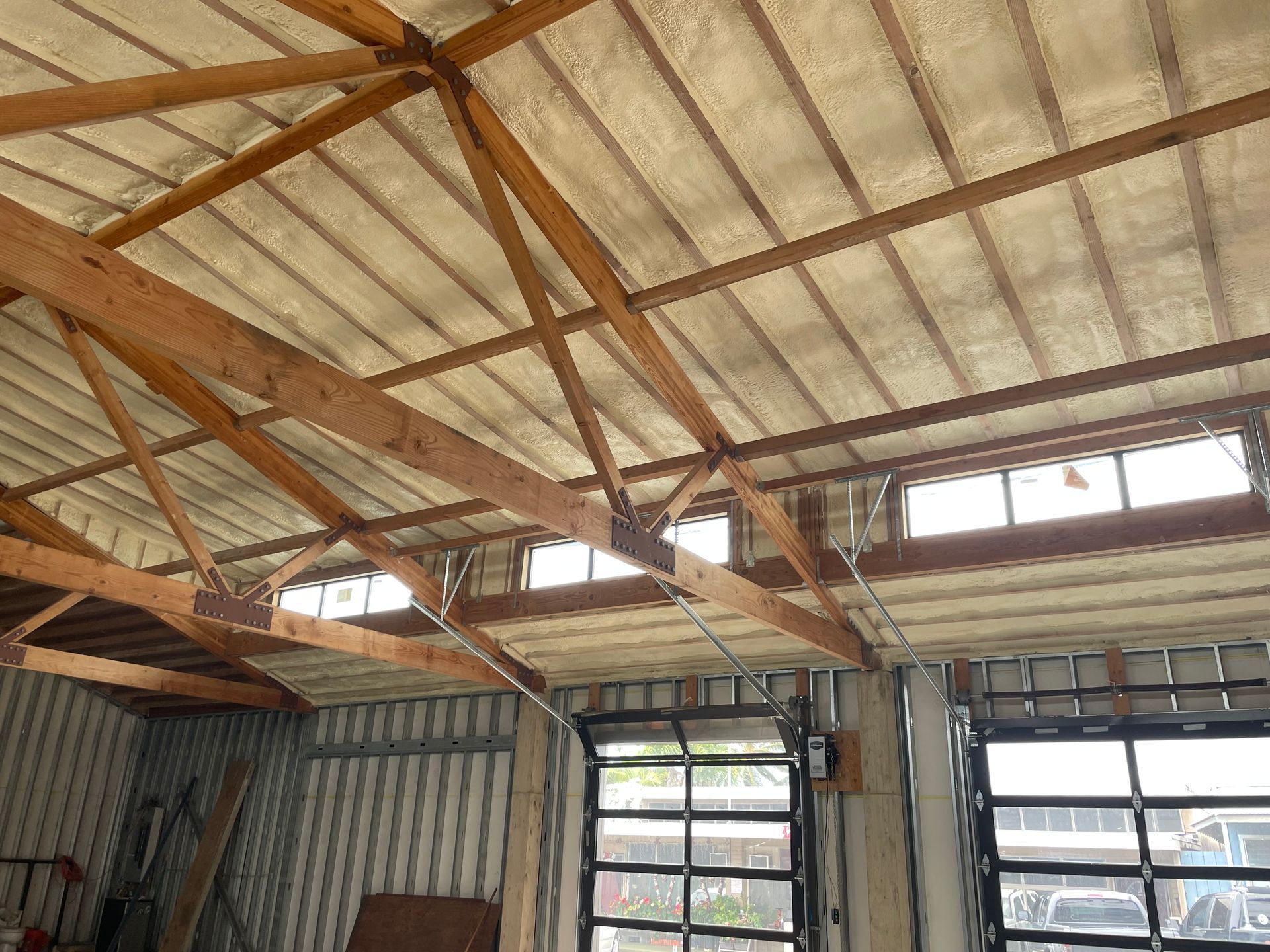 Interior view of a building with a wood and corrugated metal roof. Two glass doors are visible, and windows under the roof.